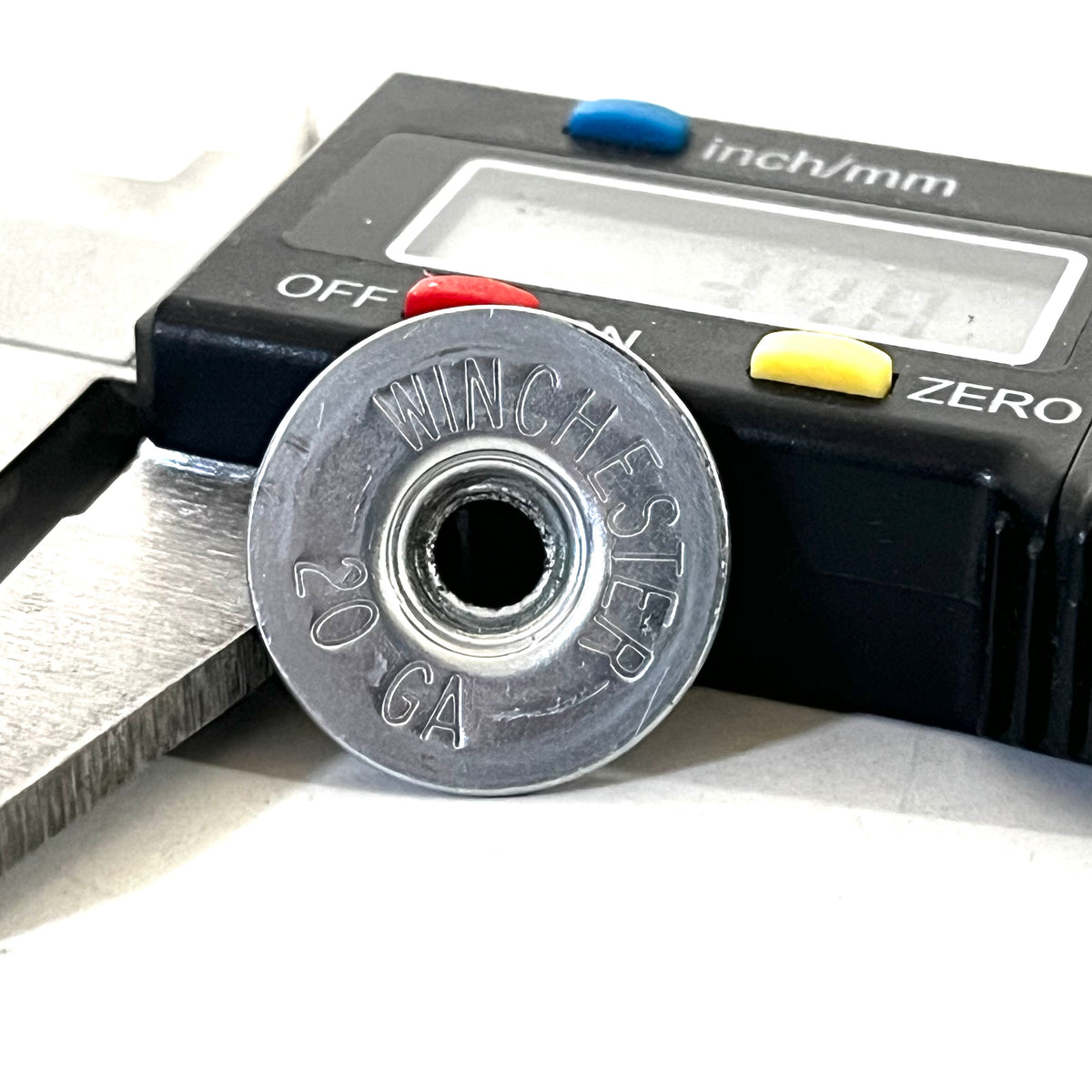 Silver Winchester 20 GA shotgun shell slice held in the jaws of a digital caliper