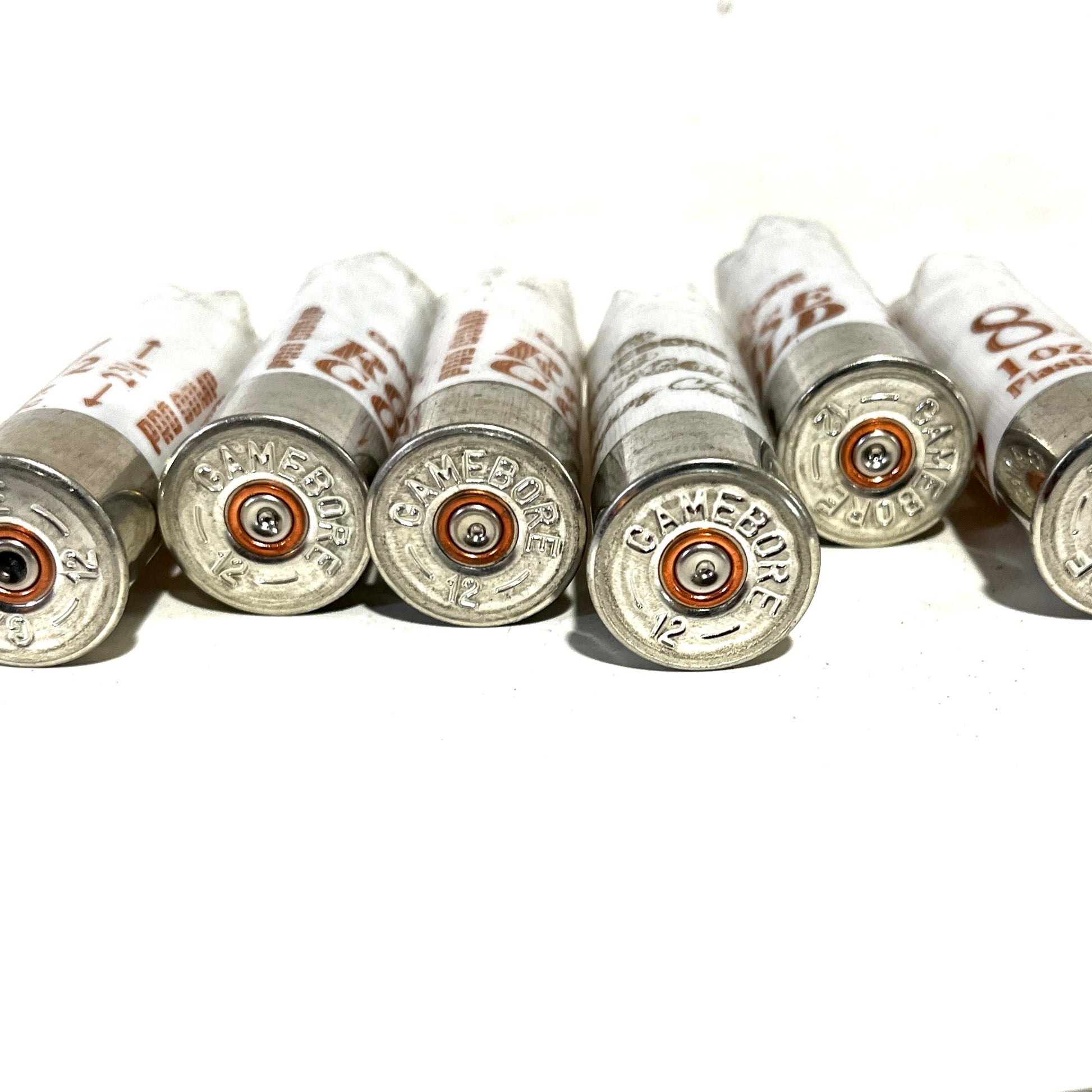 Close-up of five white Gamebore 12 gauge empty shotgun shells focusing on the headstamp silver bases with 'Gamebore' and '12' engravings, arranged in a row.
