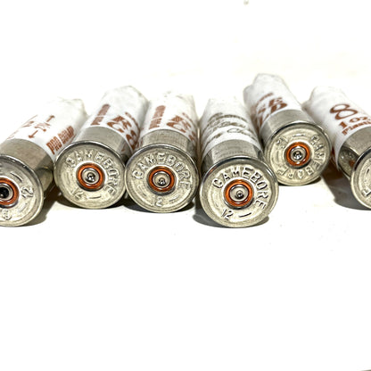 Close-up of five white Gamebore 12 gauge empty shotgun shells focusing on the headstamp silver bases with 'Gamebore' and '12' engravings, arranged in a row.

