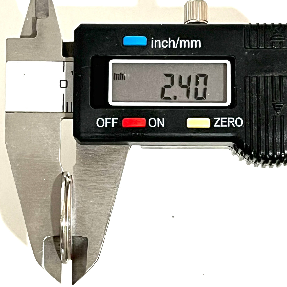 A silver shotgun shell slice measured edge-on with a digital caliper reading 2.40 mm.