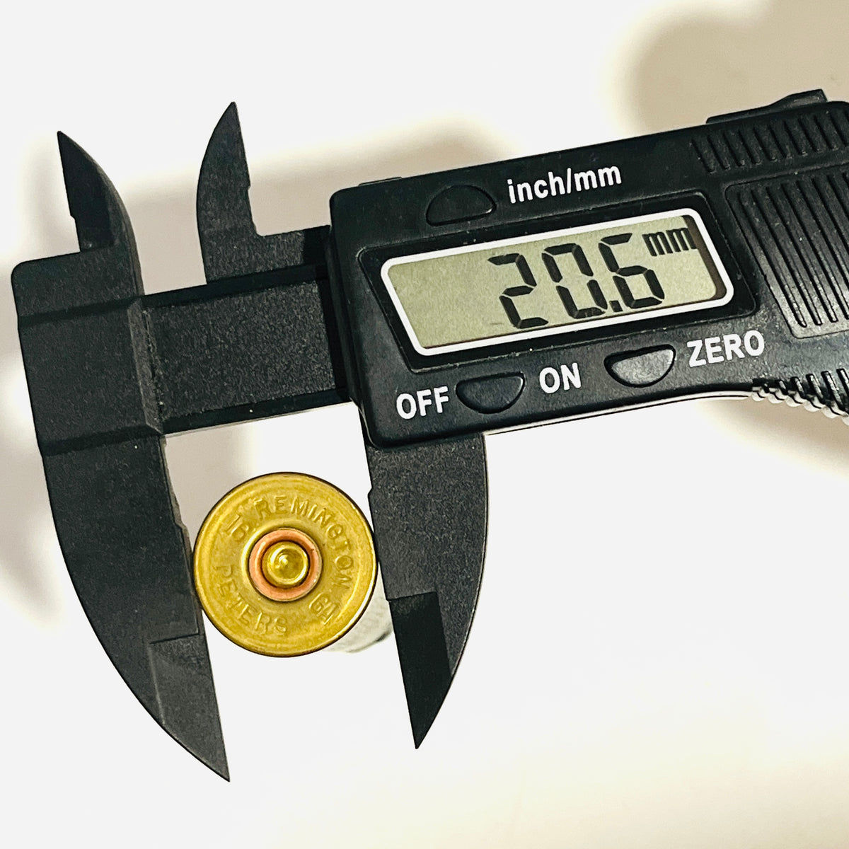 Remington Peters headstamp on a spent casing's brass base, held in a digital caliper reading 20.6 mm across