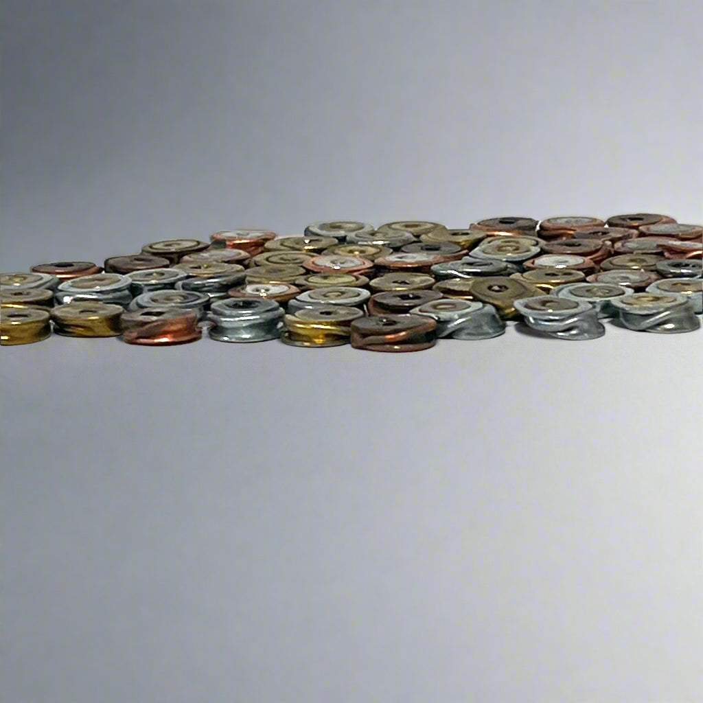 A low angle view of a flat layer of spent primer variety pack elements showing metallic edges against a plain white backdrop.