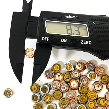 Digital caliper measuring a spent primer at 8.3 mm over a pile of spent primers on a white background.