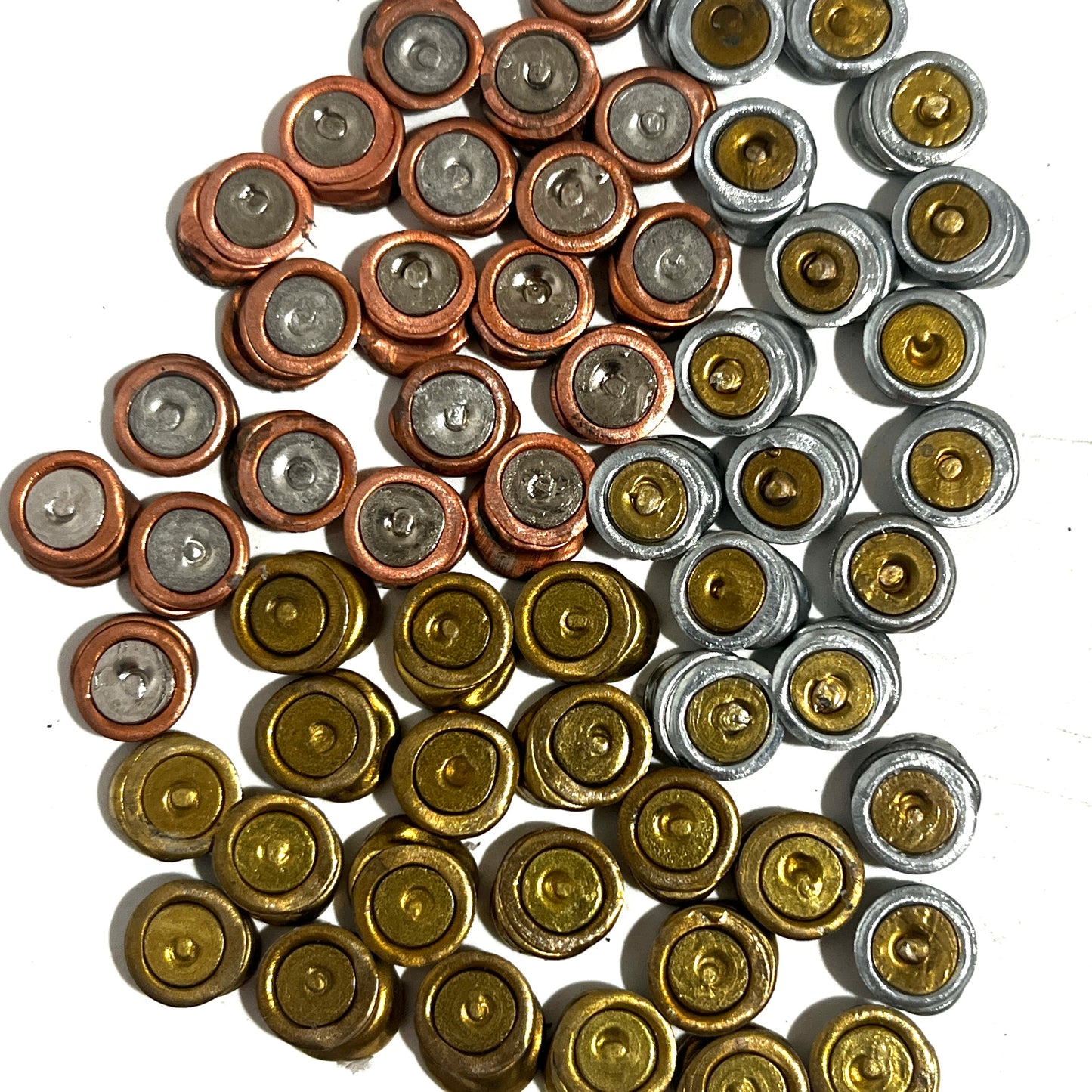 A group of spent primers flattened for earrings organized loosely by metallic colors including brass, copper, and silver on a white background.
