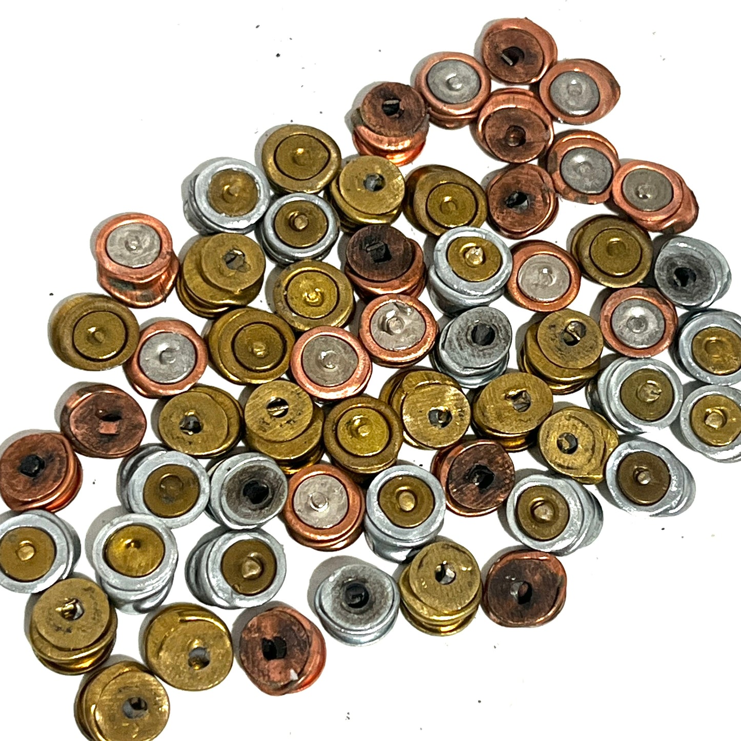 A detailed view of a random mixed cluster of spent primers in assorted metallic finishes on a white background for jewelry supplies.