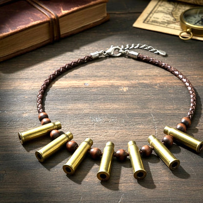 A necklace made of a braided brown leather cord, wooden beads, and 7 spent brass casings, laid on a rustic wooden table.