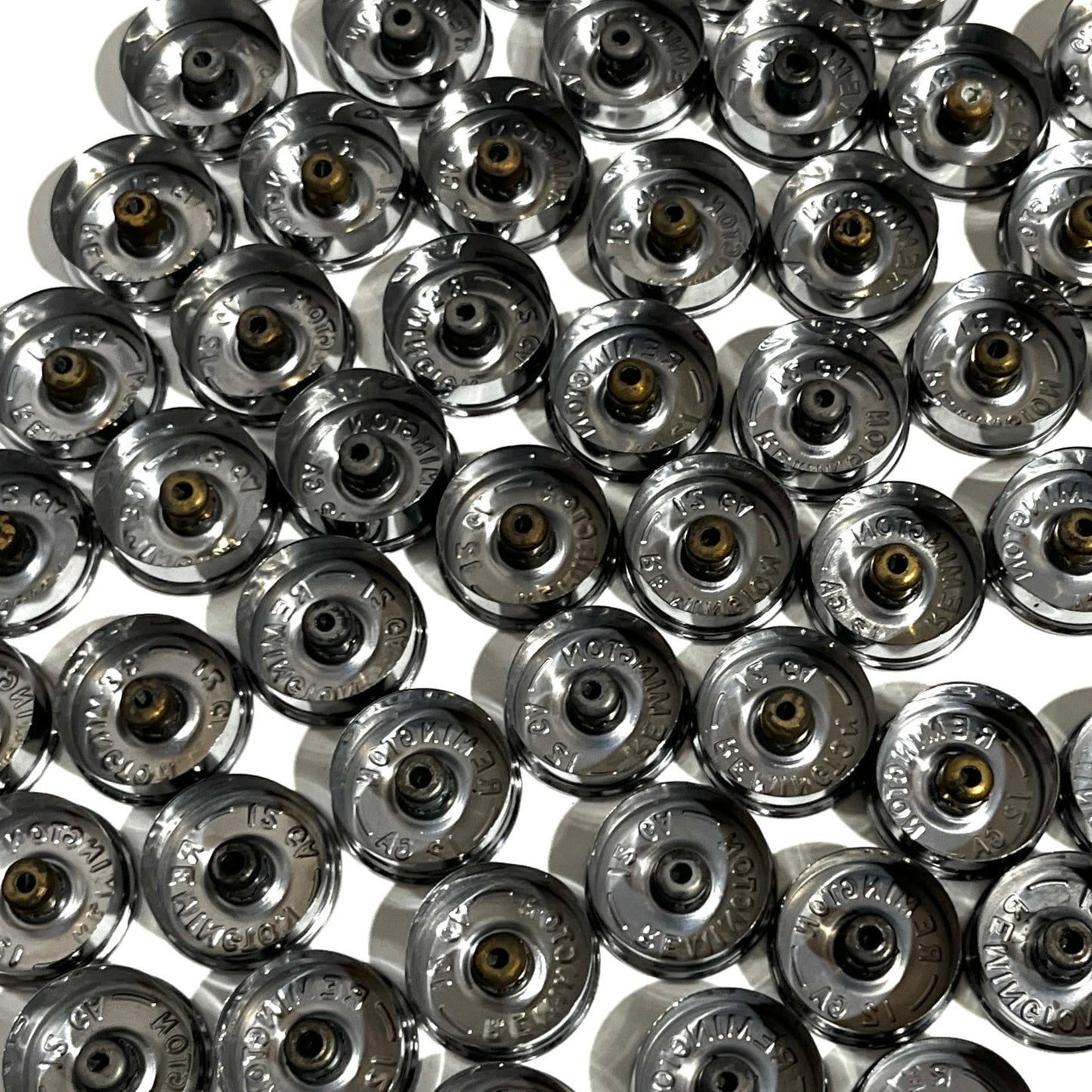 Dense group of spent silver casings resting inverted to show hollow interior undersides and intact gold primers.
