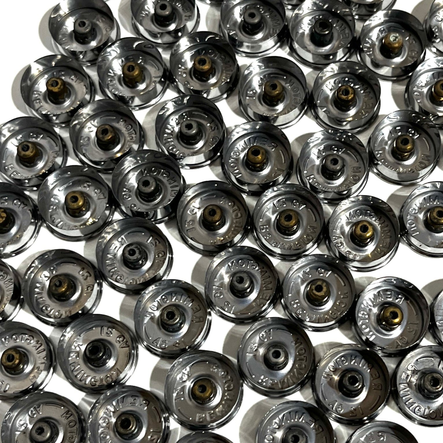 Dense group of spent silver casings resting inverted to show hollow interior undersides and intact gold primers.