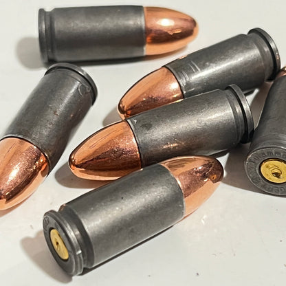 A close-up pile of gray steel 9mm dummy rounds crossed together, one gold primer visible