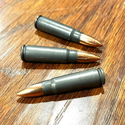 Three steel dummy cartridges with copper bullets arranged diagonally on a wood grain surface.