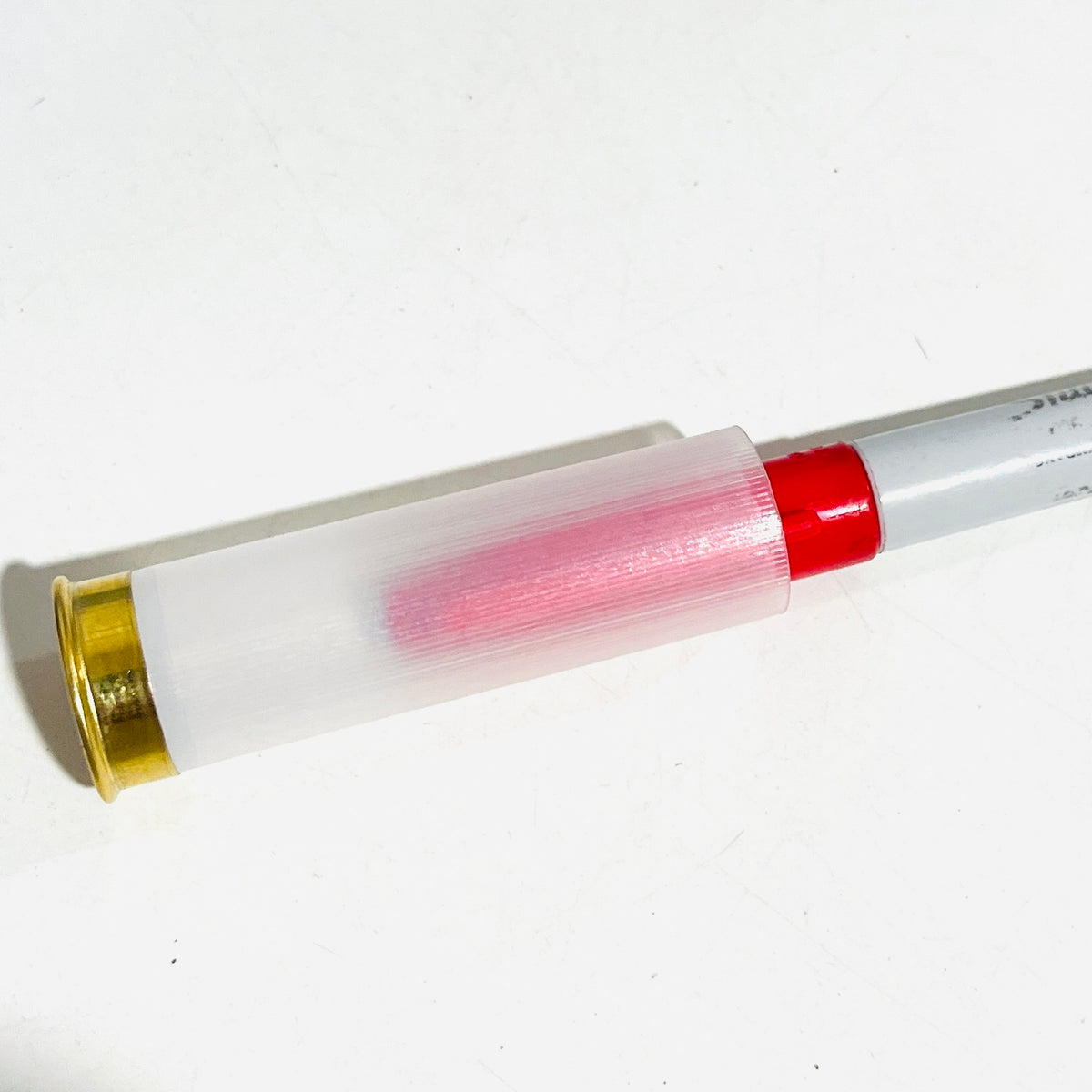 Translucent empty 12 gauge hull on its side, a red-tipped item inserted in the open end and visible through the frosted wall for comparison
