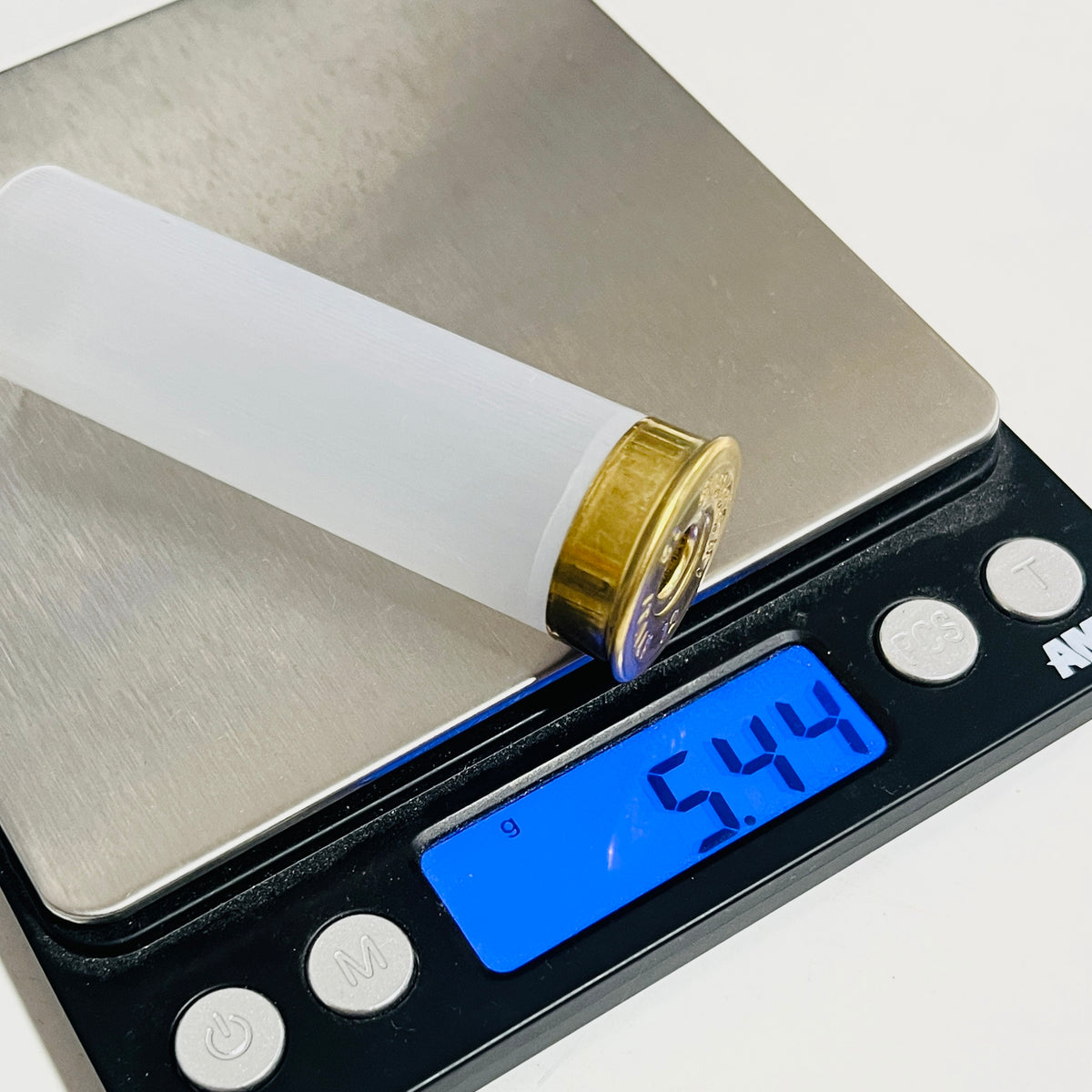 One translucent, empty 12 gauge shotgun shell resting on a digital scale reading 5.44 grams
