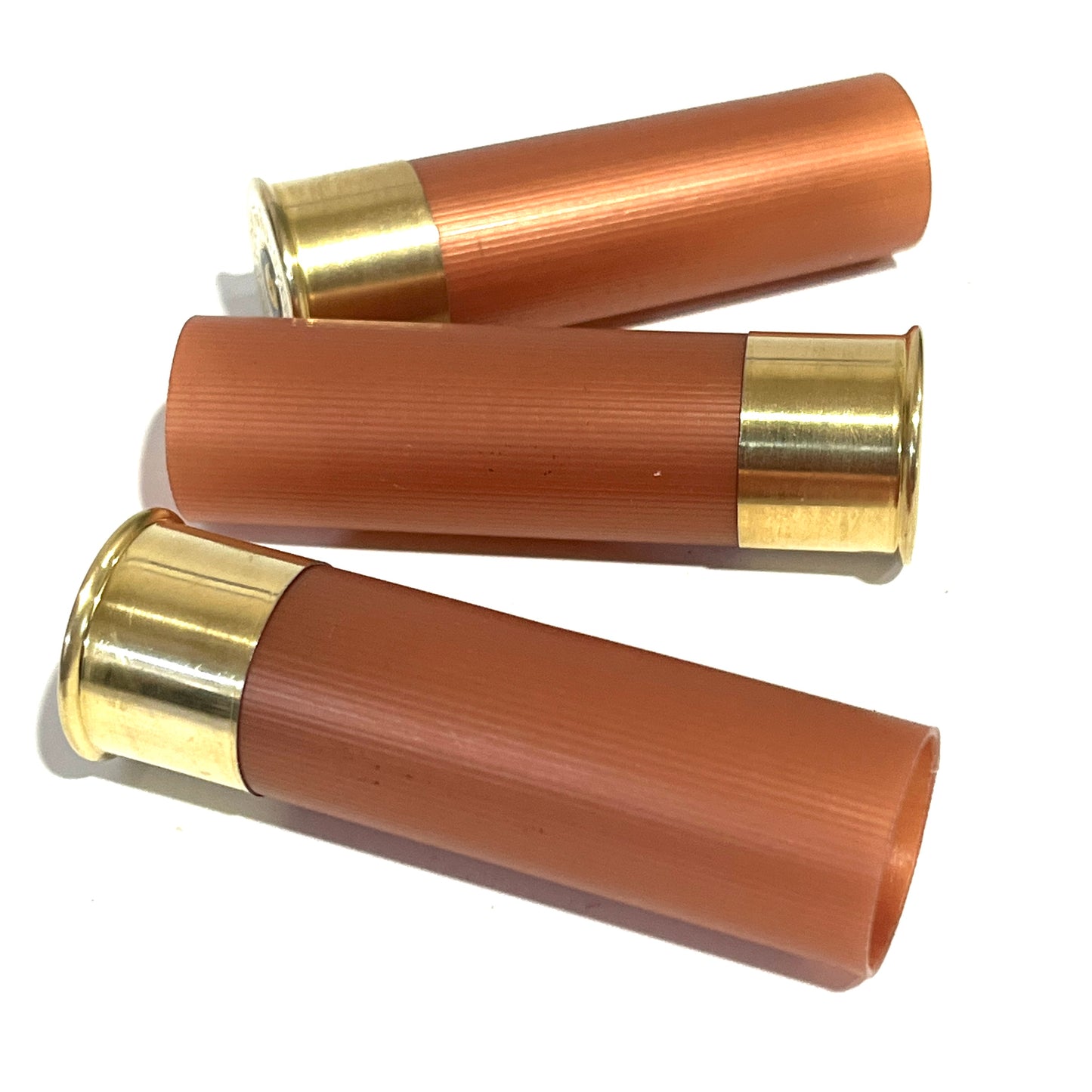 Three unmarked rose gold 12 gauge blank shotgun shells with high brass bottoms on a white background.
