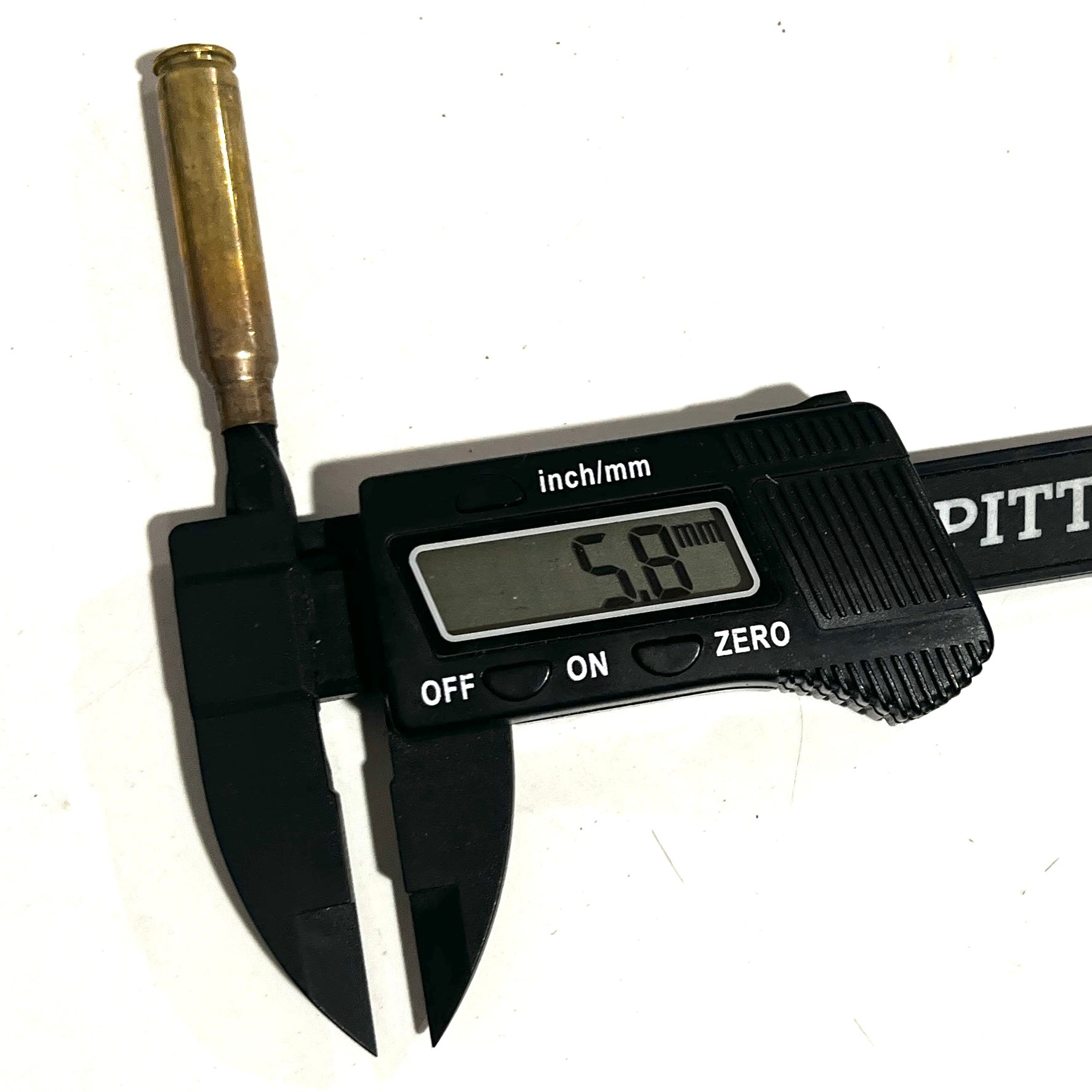 Black digital caliper measuring the neck diameter of an unpolished 223 brass casing, showing a 5.8 mm readout.