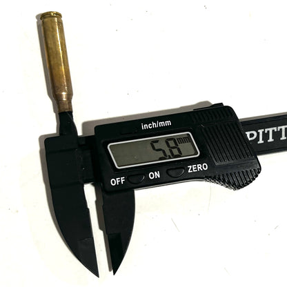 Black digital caliper measuring the neck diameter of an unpolished 223 brass casing, showing a 5.8 mm readout.