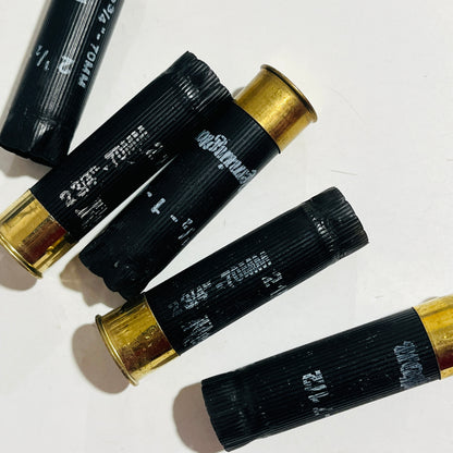 Five used black shotshells with brass bases and opened crimp ends laid diagonally on a white background
