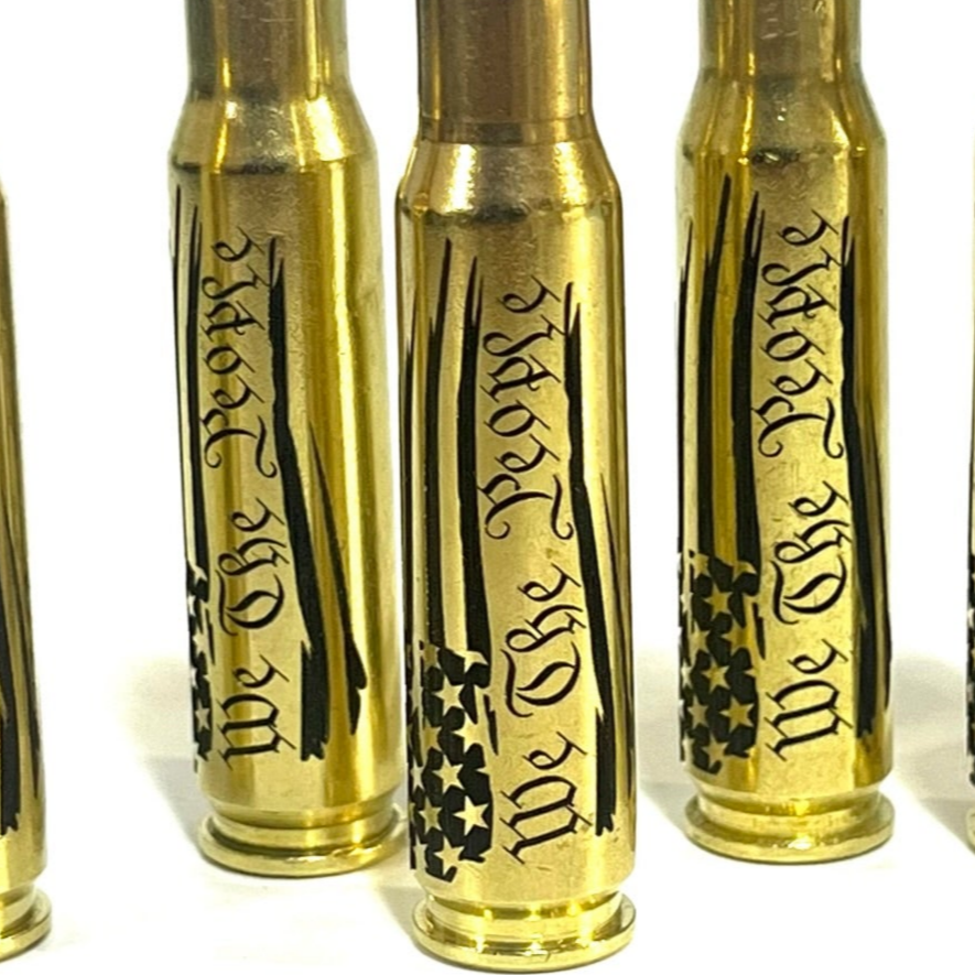 Several 'We The People' engraved brass .308 cartridges standing side by side on white