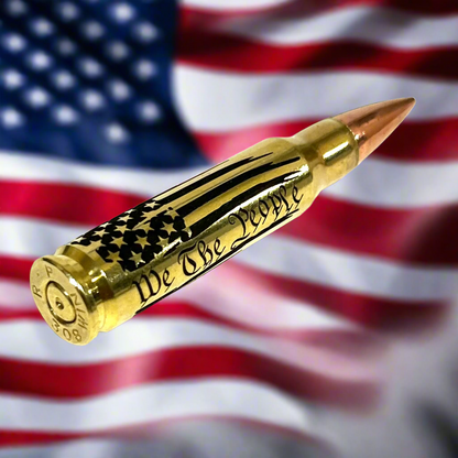 Brass .308 round engraved with 'We The People' script, styled for patriotic display against an American flag backdrop