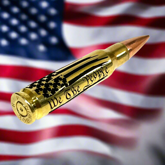 Brass .308 round engraved with 'We The People' script, styled for patriotic display against an American flag backdrop