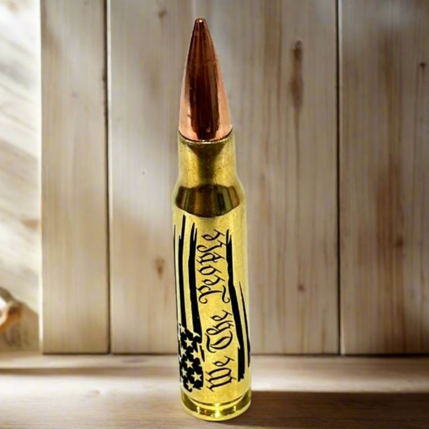 Brass .308 round with 'We The People' engraving, styled as a patriotic gift piece against a rustic wooden backdrop