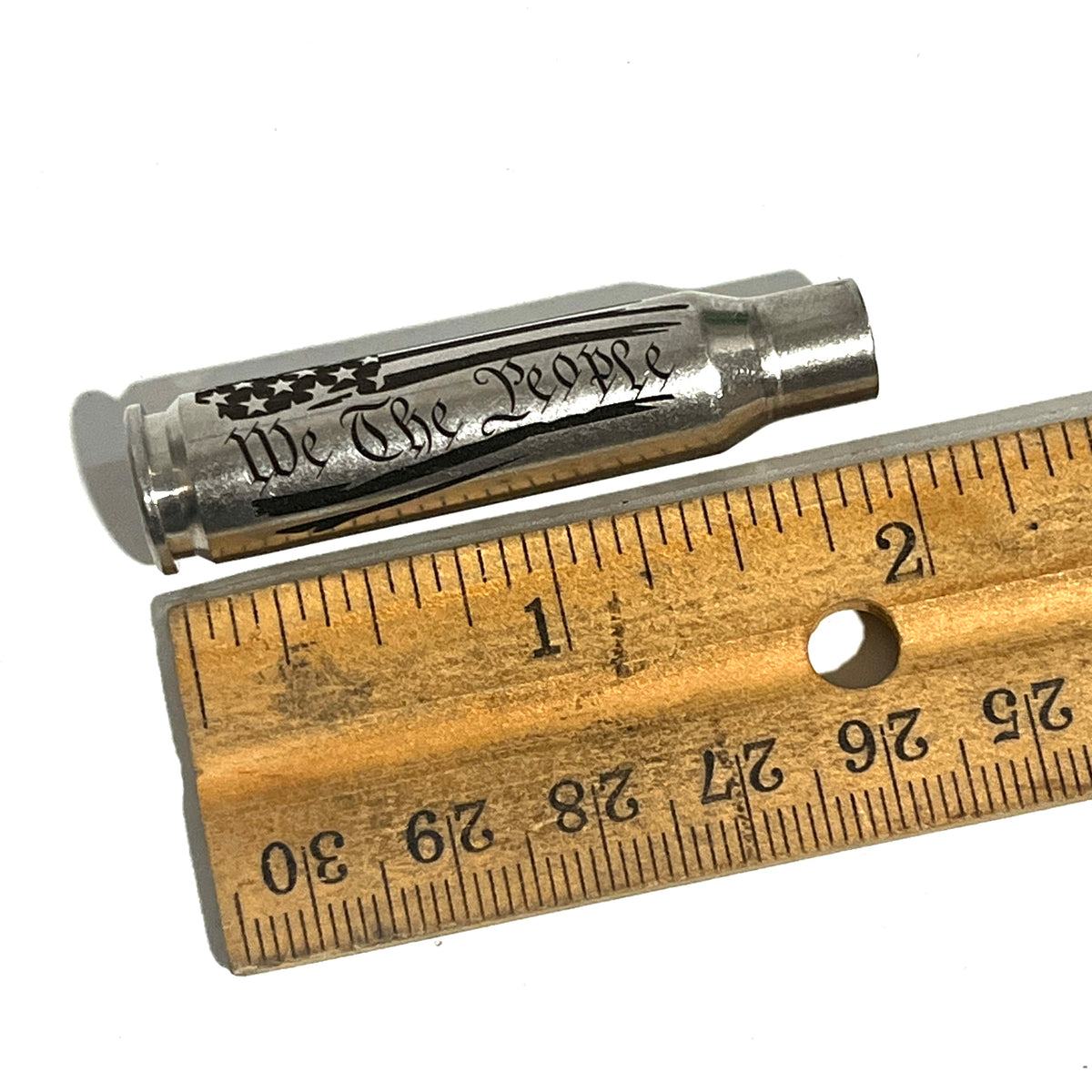 Nickel .308 WIN cartridge engraved with We The People next to a wooden ruler for scale