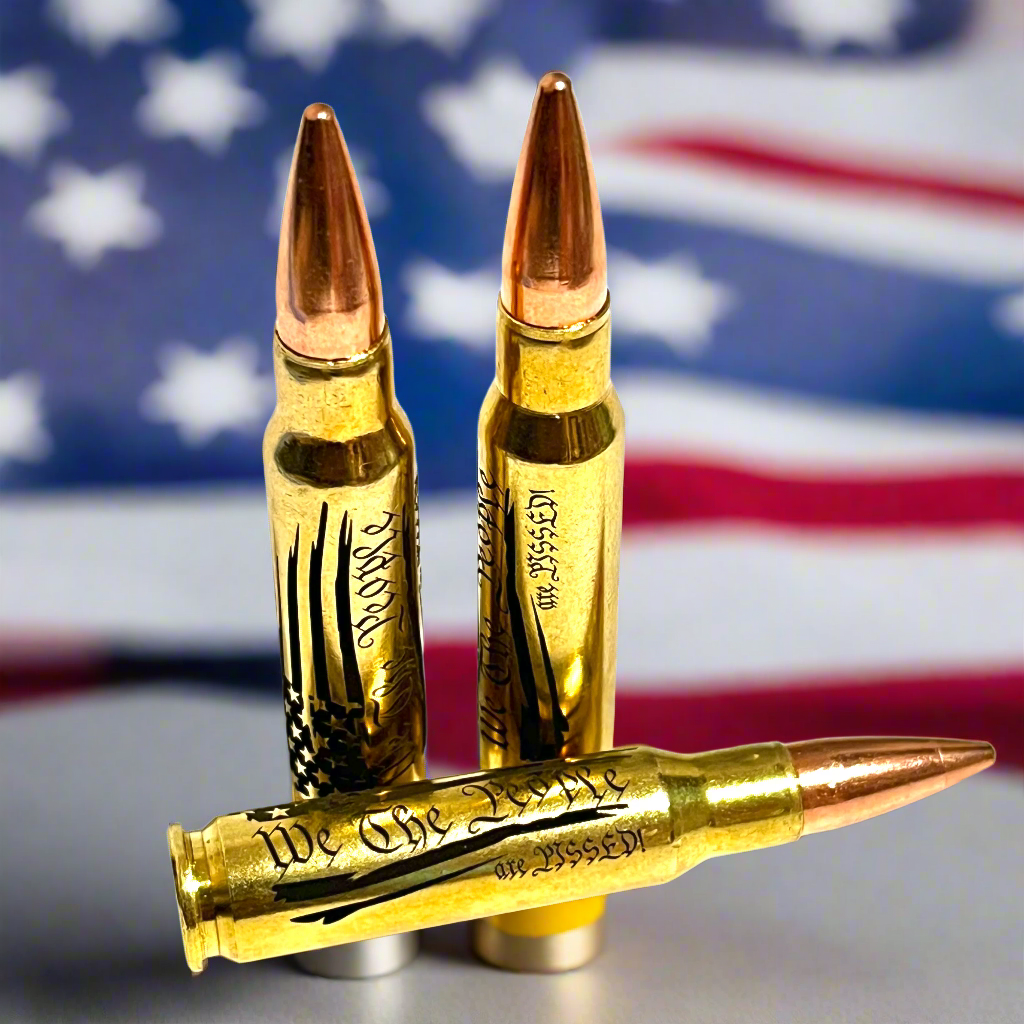3 brass .308 WIN cartridges engraved with 'We The People Are Pissed' in front of a blurred American flag