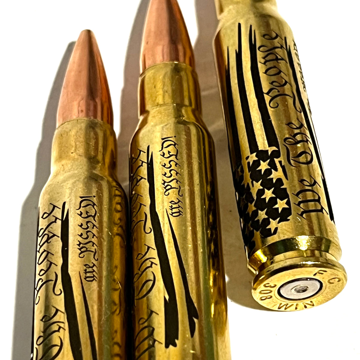 3 brass .308 WIN cartridges engraved with 'We The People Are Pissed', close-up on headstamps reading 308 WIN