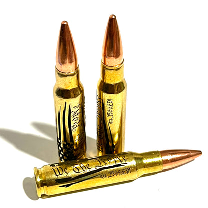 3 brass .308 WIN cartridges engraved with 'We The People Are Pissed' and copper bullet tips, white background