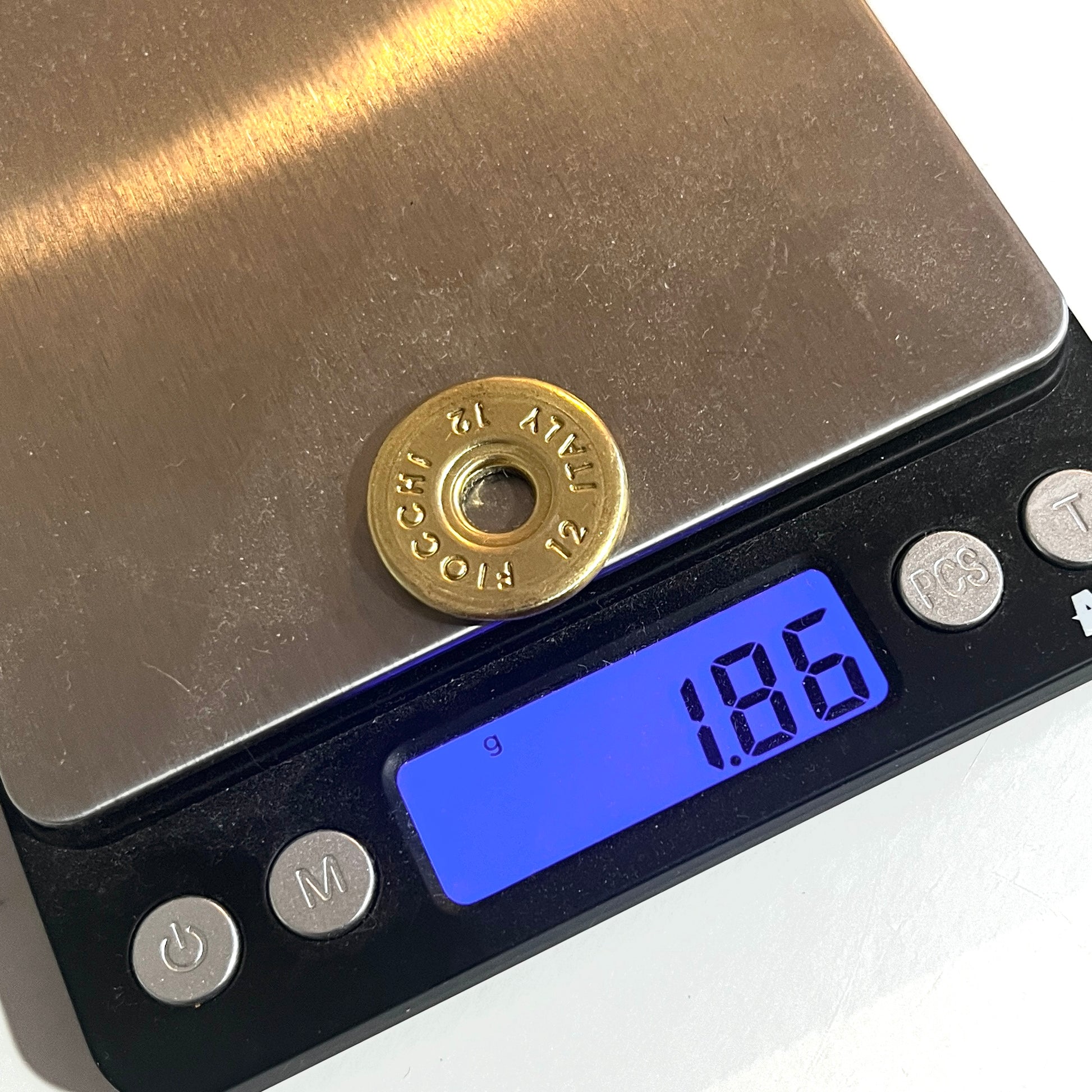 Round brass 12 gauge Fiocchi Italy headstamp slice on a digital scale reading 1.86 grams
