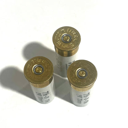 Three white Federal 12 gauge dummy shotgun shells viewed base-up showing gold primers on a white background