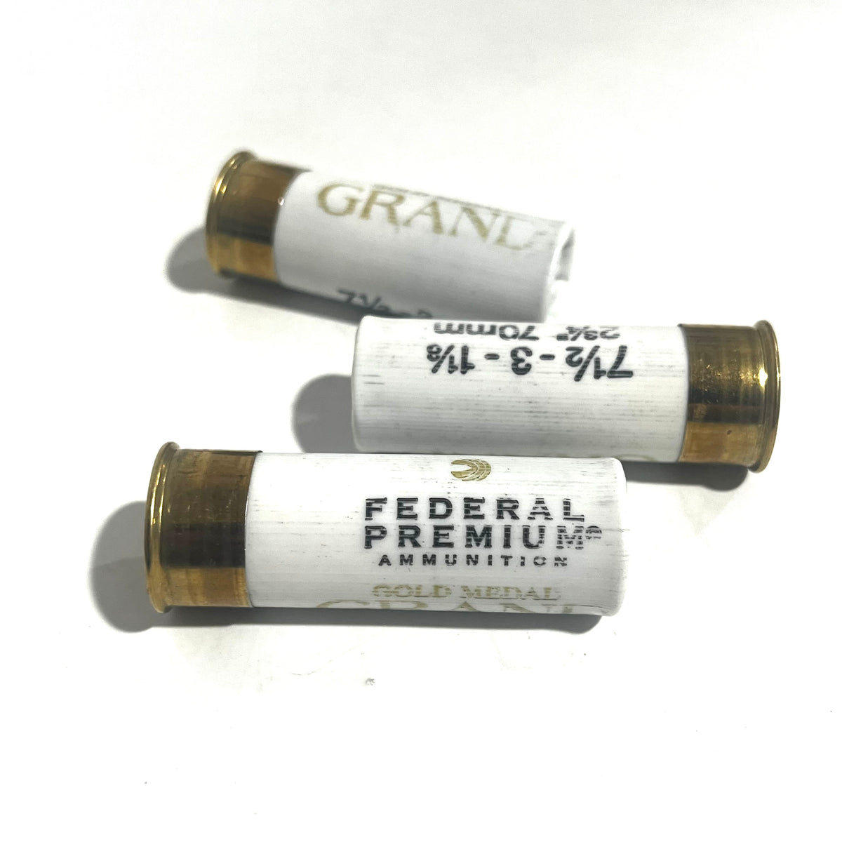 Three white Federal Premium Gold Medal Grand 12 gauge dummy shotgun shells with gold bases on a white background