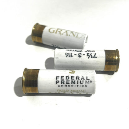 Three white Federal Premium Gold Medal Grand 12 gauge dummy shotgun shells with gold bases on a white background