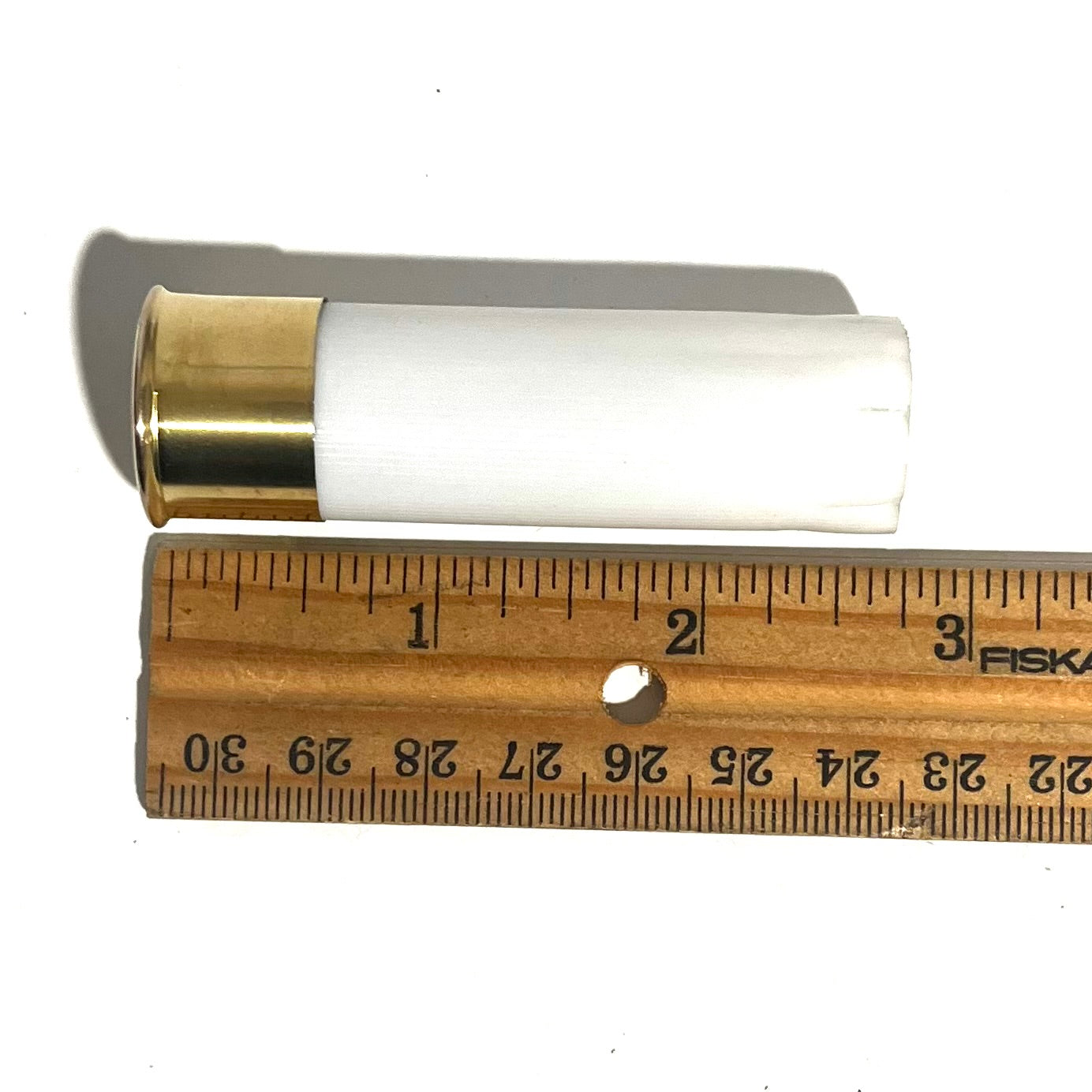 White 12 gauge blank shotgun shell with brass base measured against a ruler showing approximately 2.75 inches