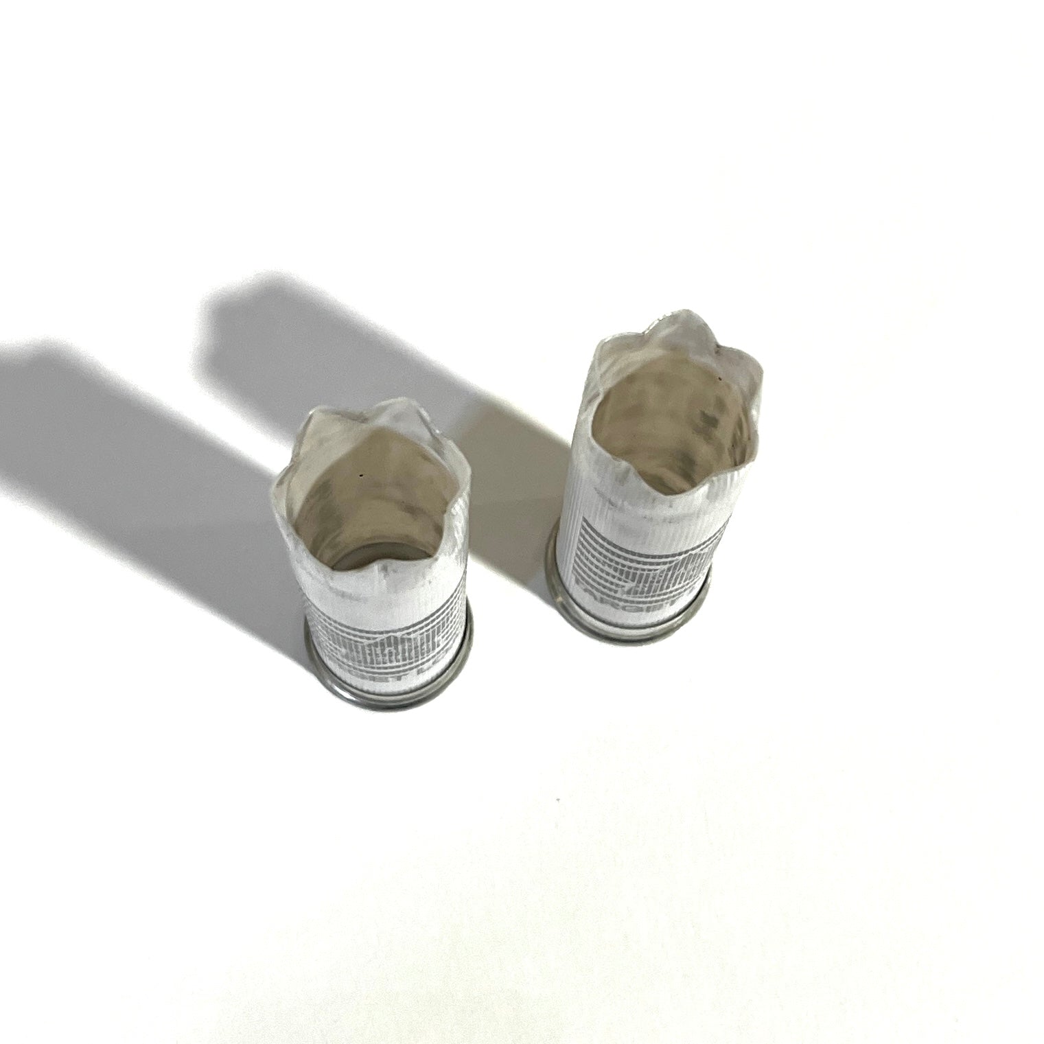 Two white 12 gauge empty shotgun shells viewed open-end up showing torn crimped mouths on a white background
