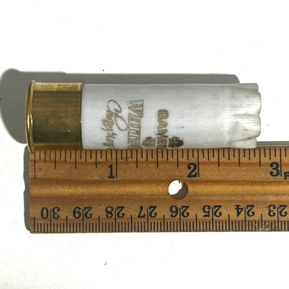 White Gamebore 12 gauge empty shotgun shell with a gold base laid next to a wooden ruler showing a length of about 2.75 inches