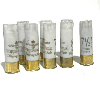 Six white 12 gauge empty shotgun shells with gold brass bases printed Gamebore White Gold standing upright on a white background