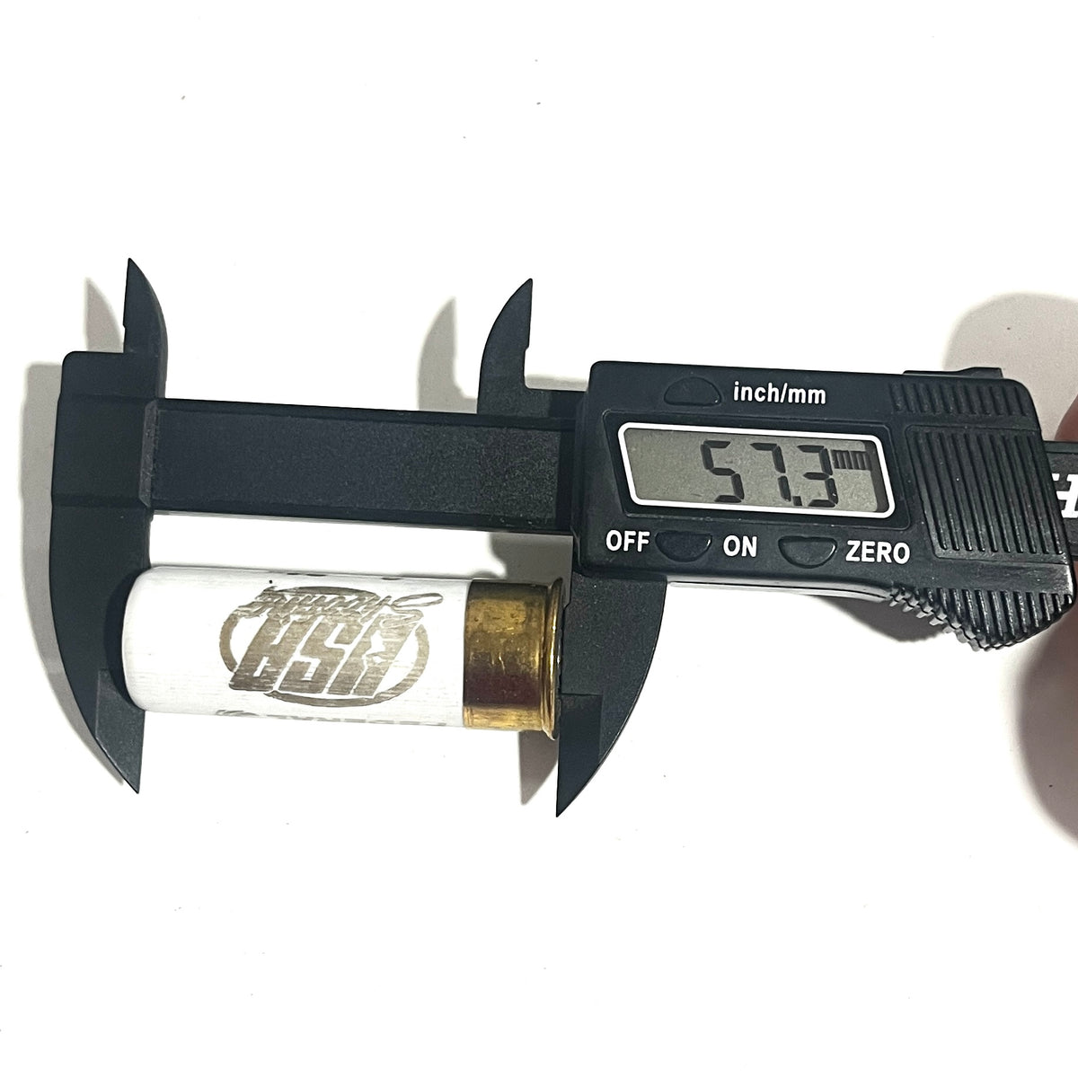 A white once-fired shell with USA Shooting text being measured for diameter with a black digital caliper reading 57.3.