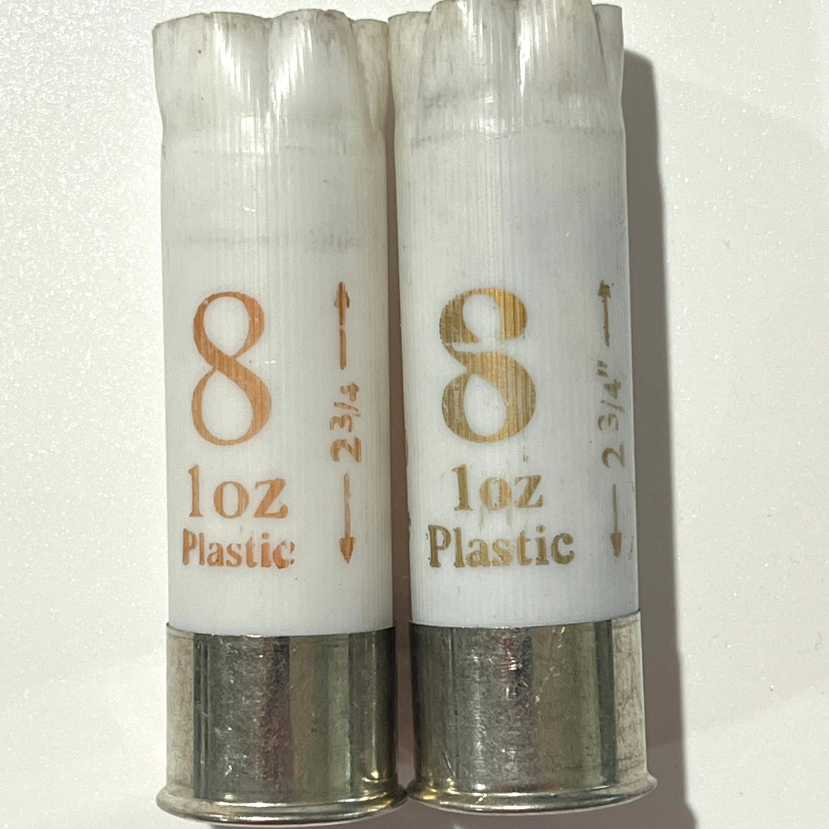 Two plastic white shotgun shells 12 gauge empty labeled '8 oz Plastic' with metallic silver bases, shown side by side on a white background.