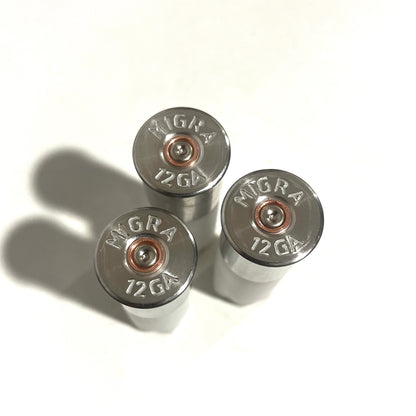3 silver shotgun shell base caps stamped MIGRA 12GA with copper primers, viewed from above