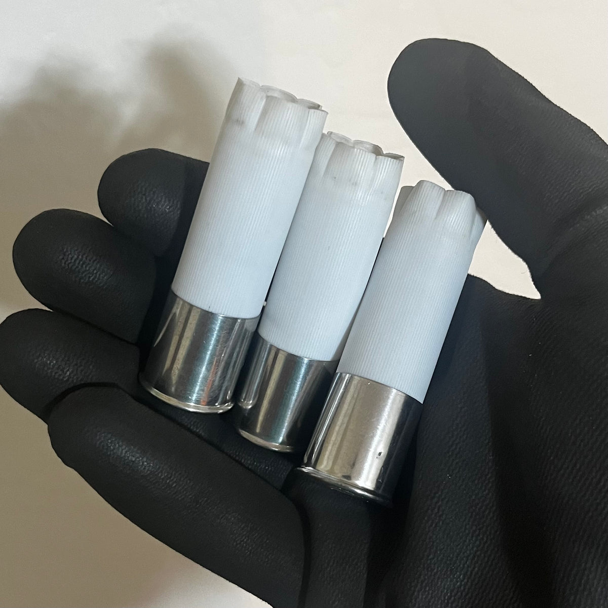 3 white shotgun shell hulls with silver high brass bases held in a gloved hand