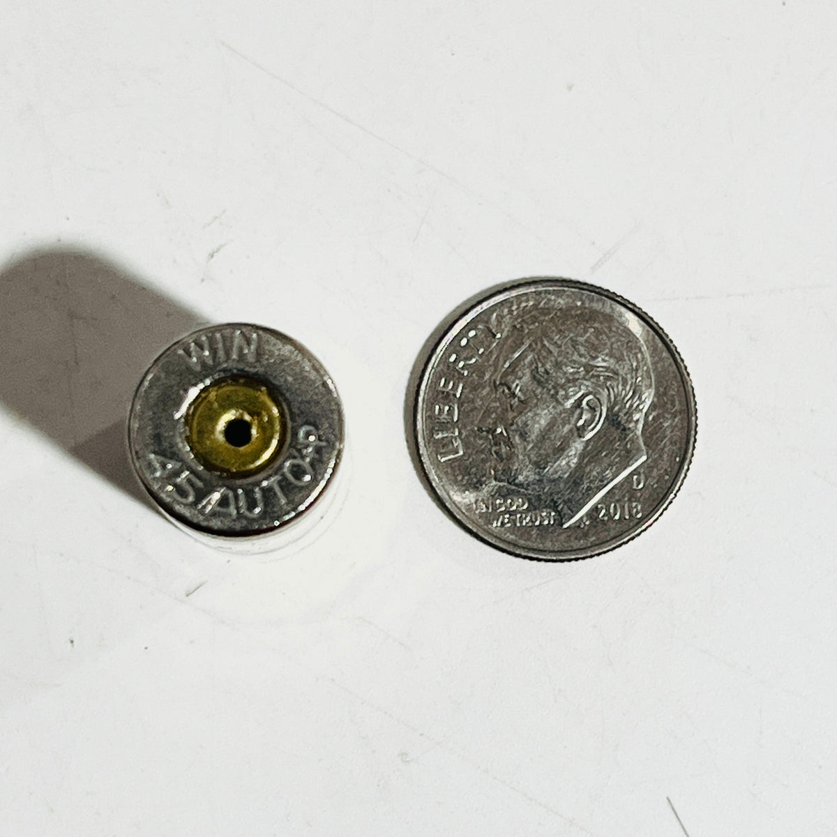 WIN 45 Auto +P headstamp on an empty nickel case with a drilled primer, shown beside a dime for size