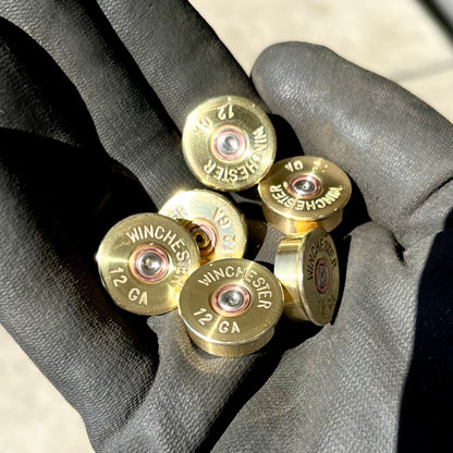 5 gold brass shell heads with "Winchester 12 GA" headstamps held in a gloved hand
