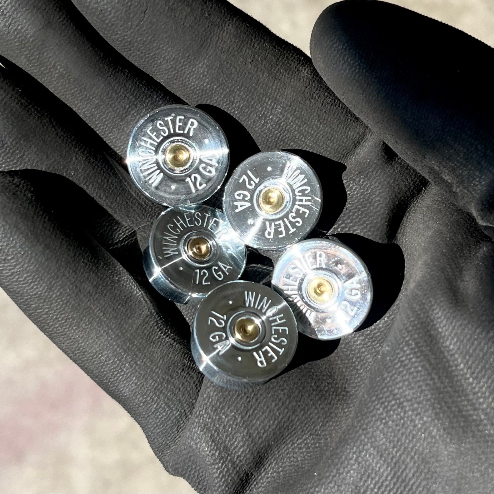 Gloved hand holding five hand-polished Winchester 12 gauge steel shotgun shell headstamps