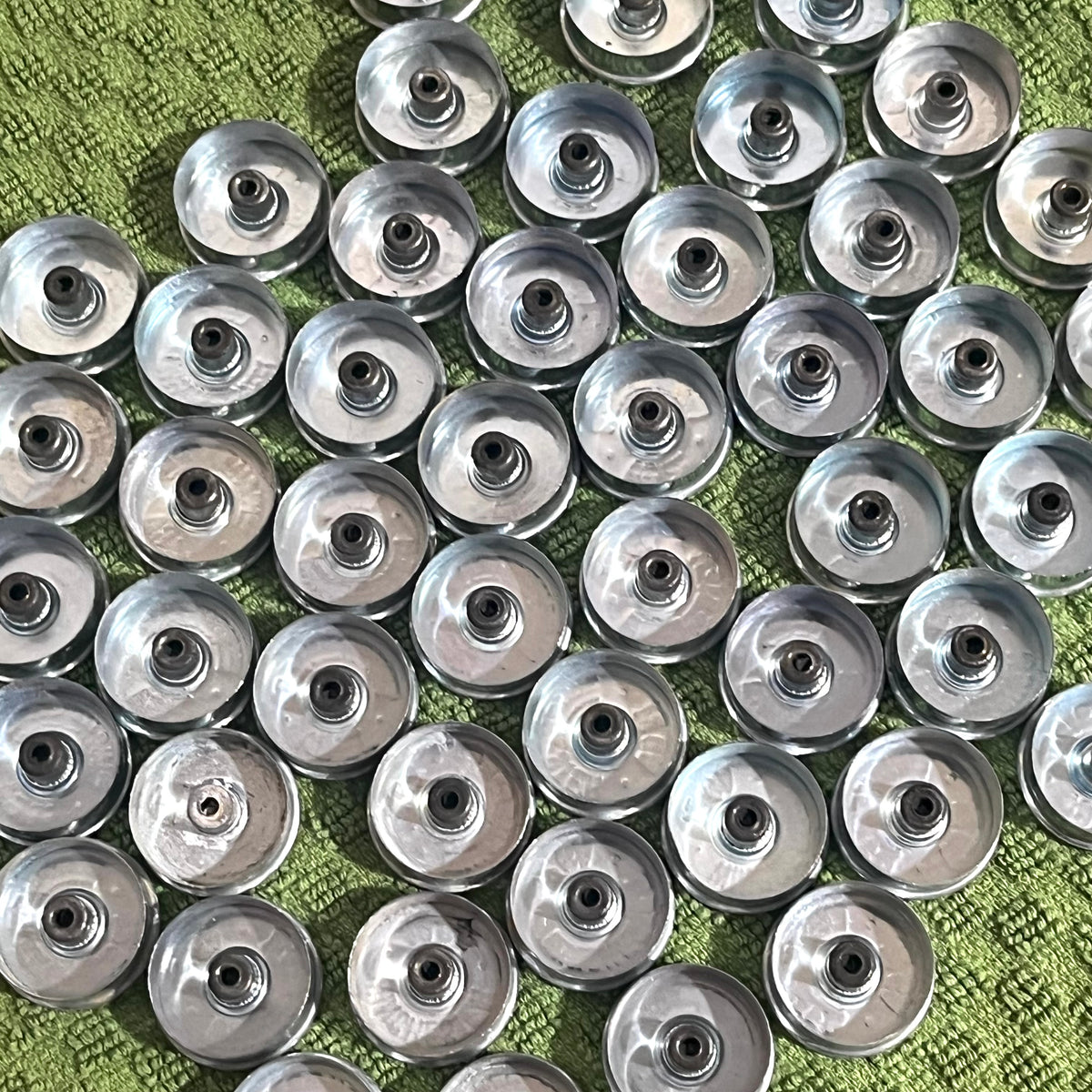 Rows of silver Winchester 12 gauge steel headstamps arranged closely together on a green fabric background, viewed from above showing gold primers