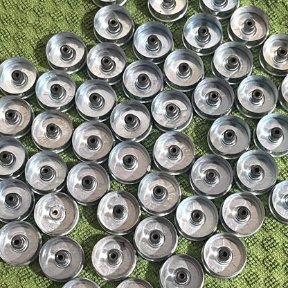 Rows of silver Winchester 12 gauge steel headstamps arranged closely together on a green fabric background, viewed from above showing gold primers