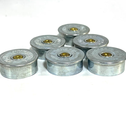 Six silver Winchester 12 gauge steel headstamps standing upright on a white background, showing gold primers and ‘Winchester’ stampings