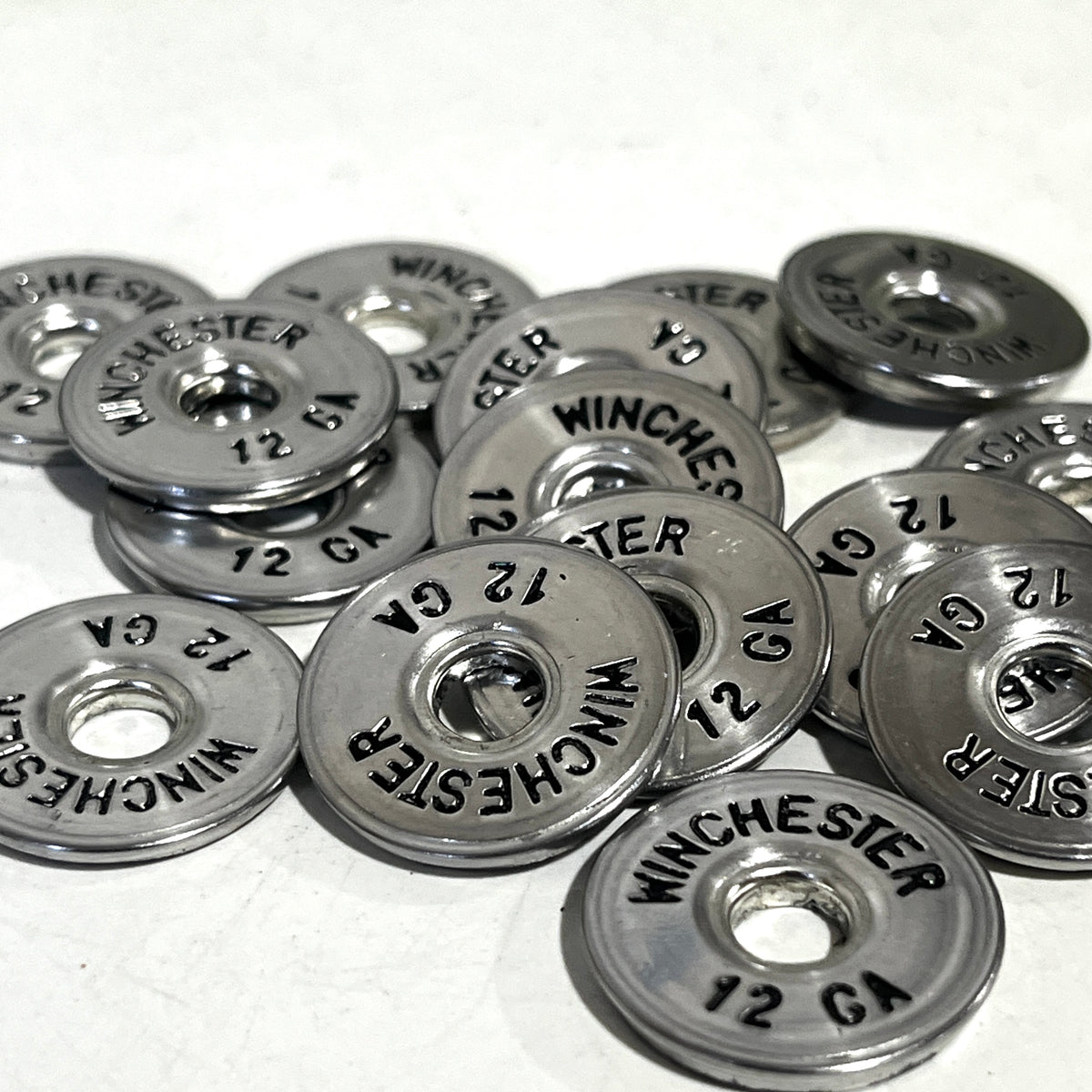 A pile of silver Winchester 12 gauge slices hand painted black scattered on a white surface.