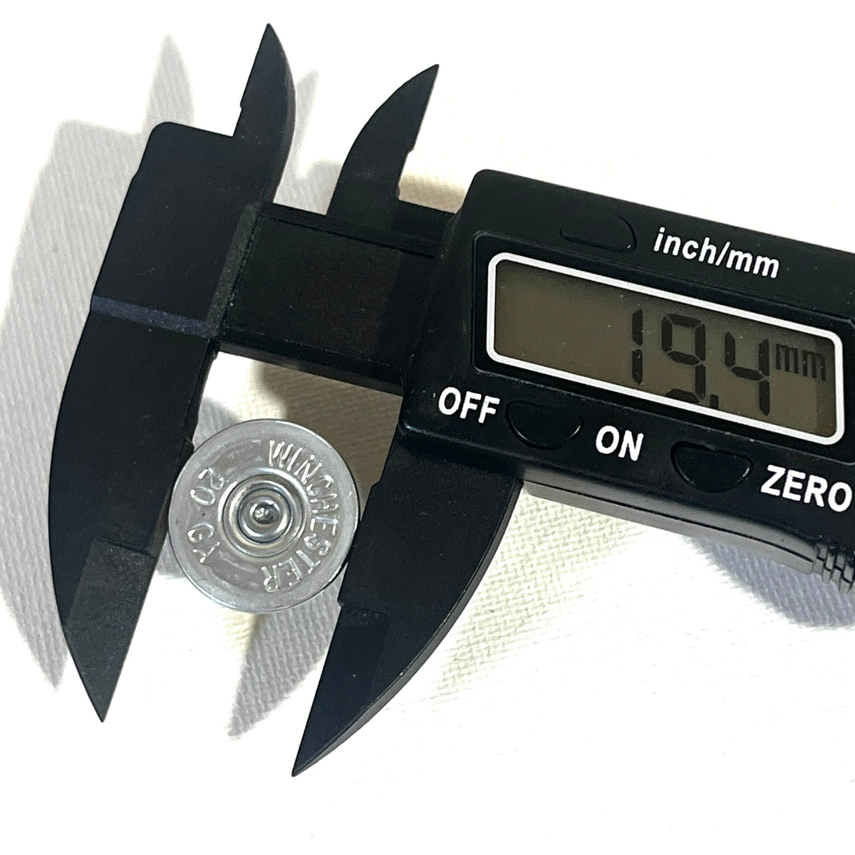 Digital caliper measuring the diameter of a silver Winchester 20 gauge shotgun shell slice at 19.4 millimeters