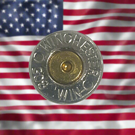 Close-up of a Winchester 308 nickel bullet slice with gold primer, in front of a blurred American flag