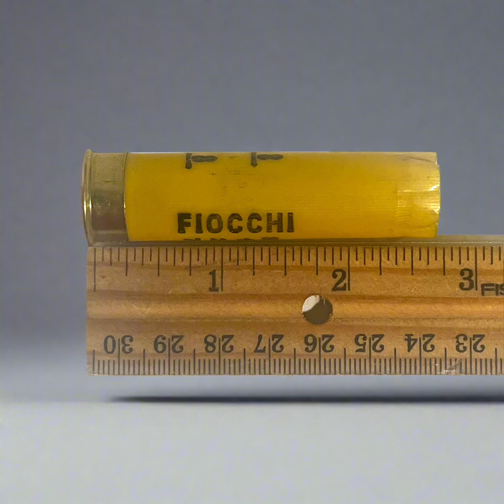 Yellow Fiocchi shotgun shell hull measured on a wooden ruler at approximately 2.75 inches